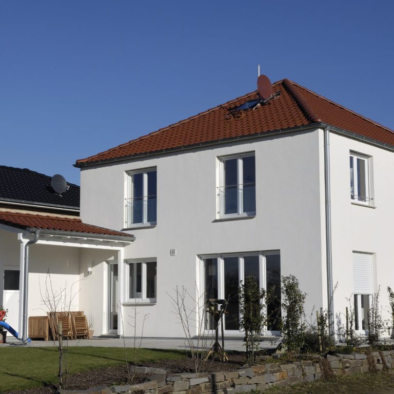 Helles, modernes Einfamilienhaus mit rotem Dach und Garten.